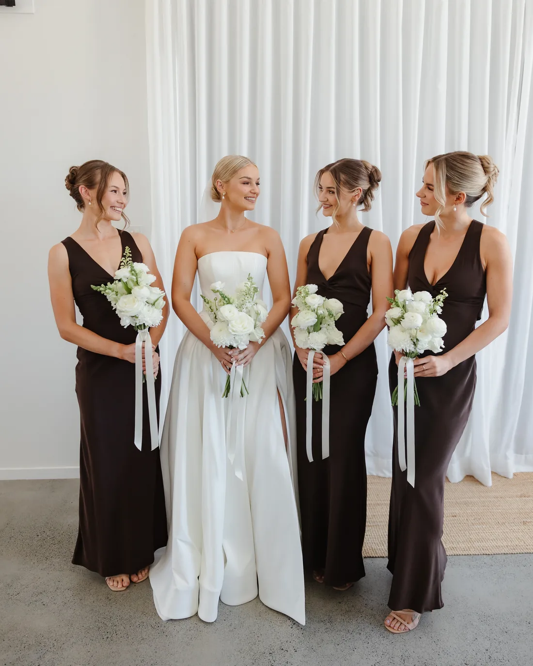 Bride with her three bridesmaids in chocolate brown gowns, holding white bouquets