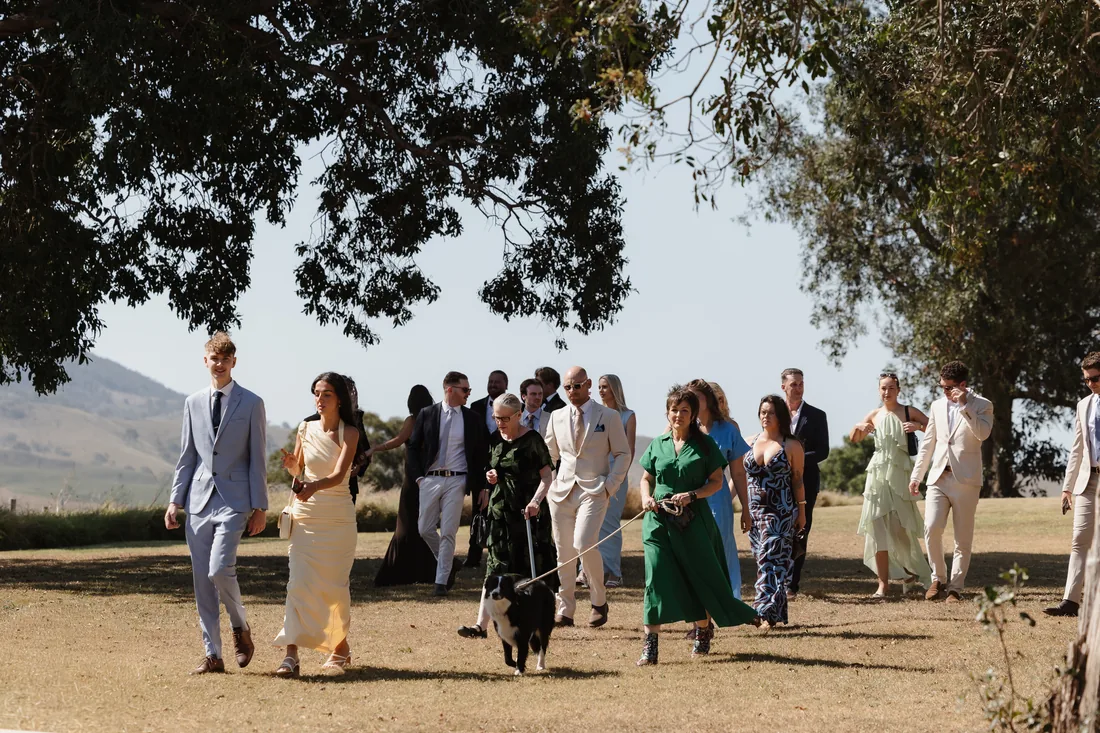Guests walking to the ceremony with a dog on a lead, mountain views behind