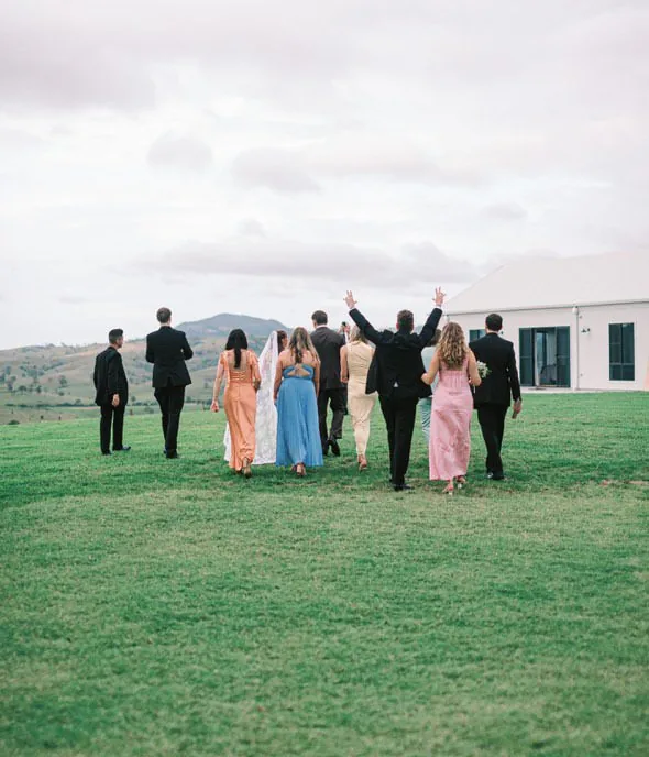 Bridal party walking across the lawn towards the reception, arms raised