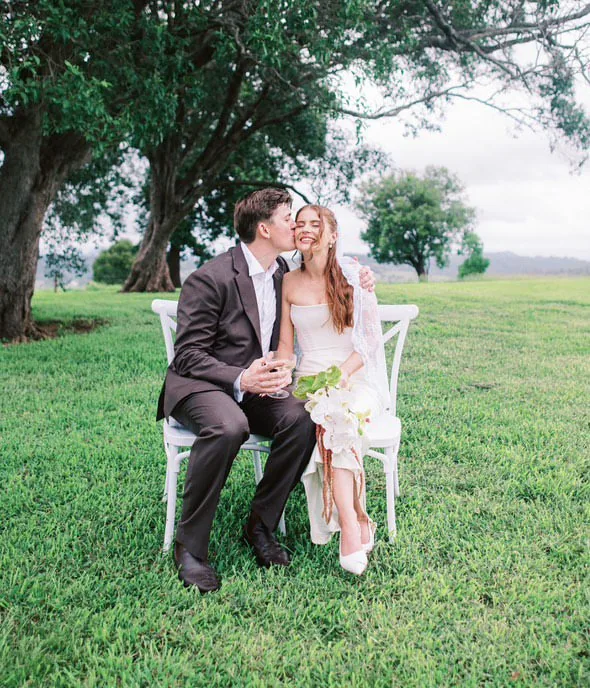 Alex and Will sharing a kiss seated together under a tree