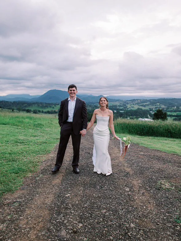 Alex and Will holding hands walking down the gravel driveway with mountain views