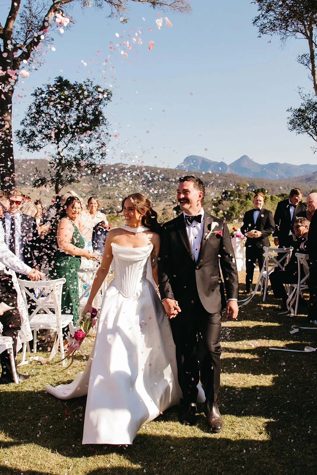 Ally and Braydon walking back down the aisle through confetti as guests celebrate