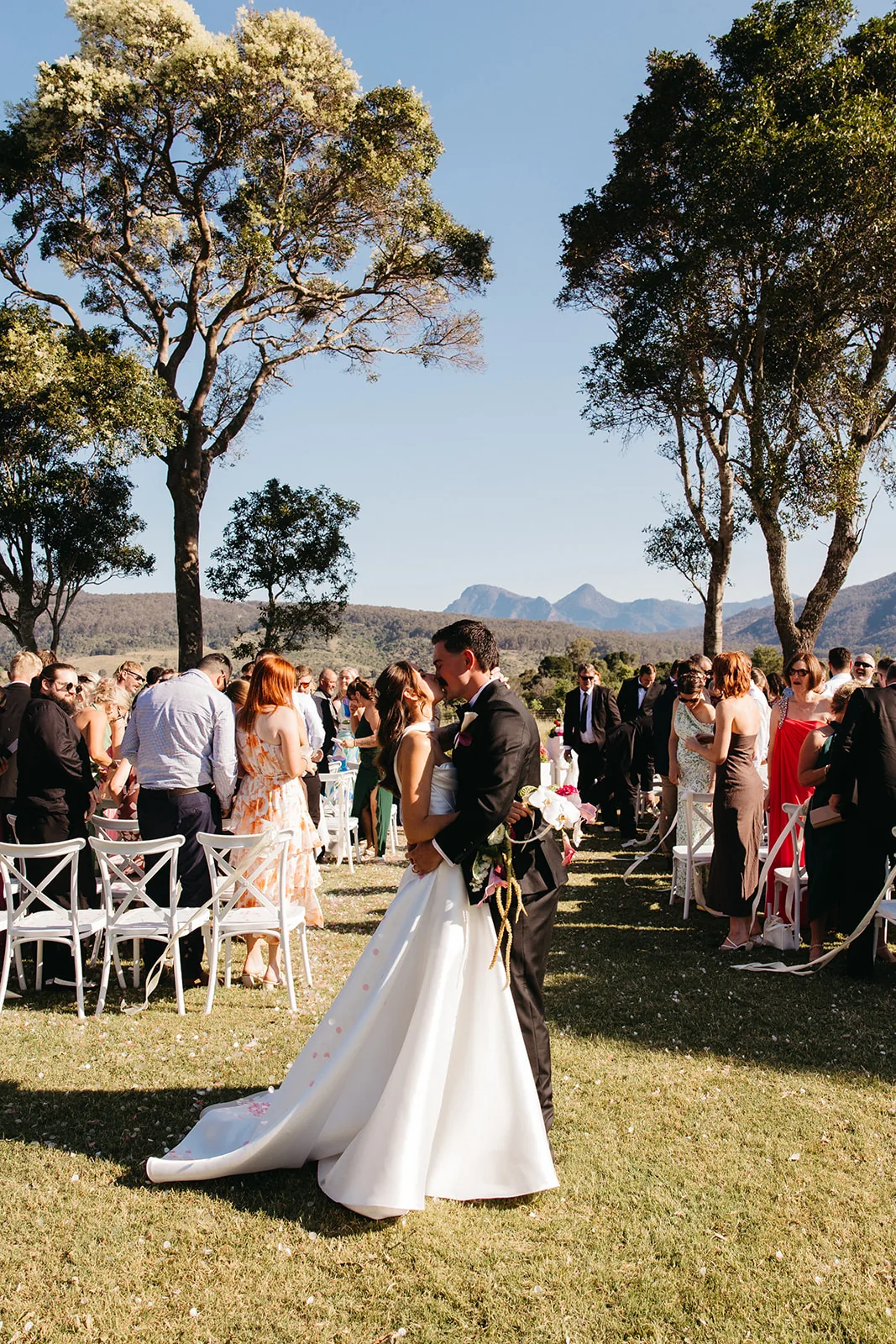 Ally and Braydon kissing among guests after the ceremony, mountain views behind