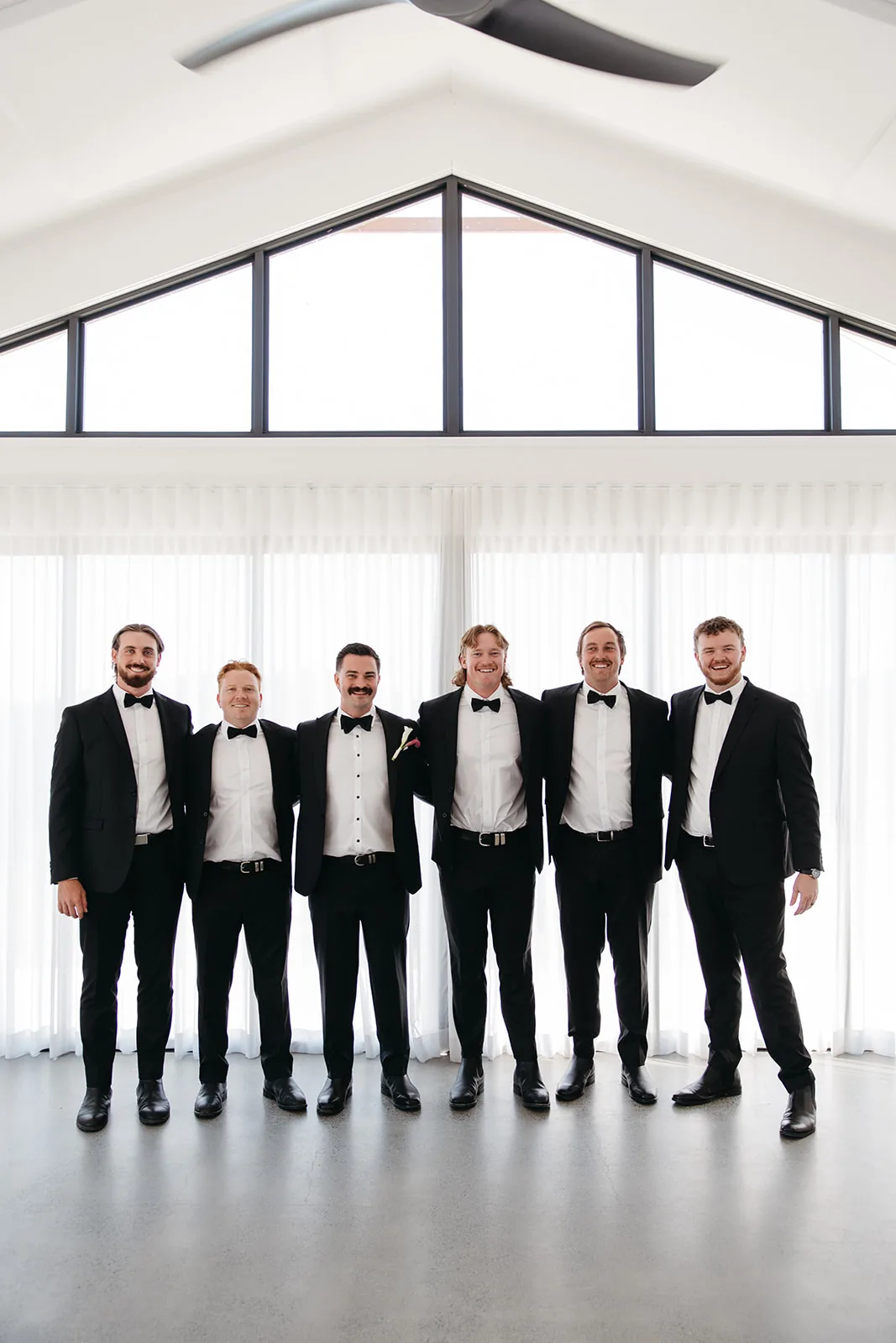 Groomsmen group photo in black tuxedos inside the reception building
