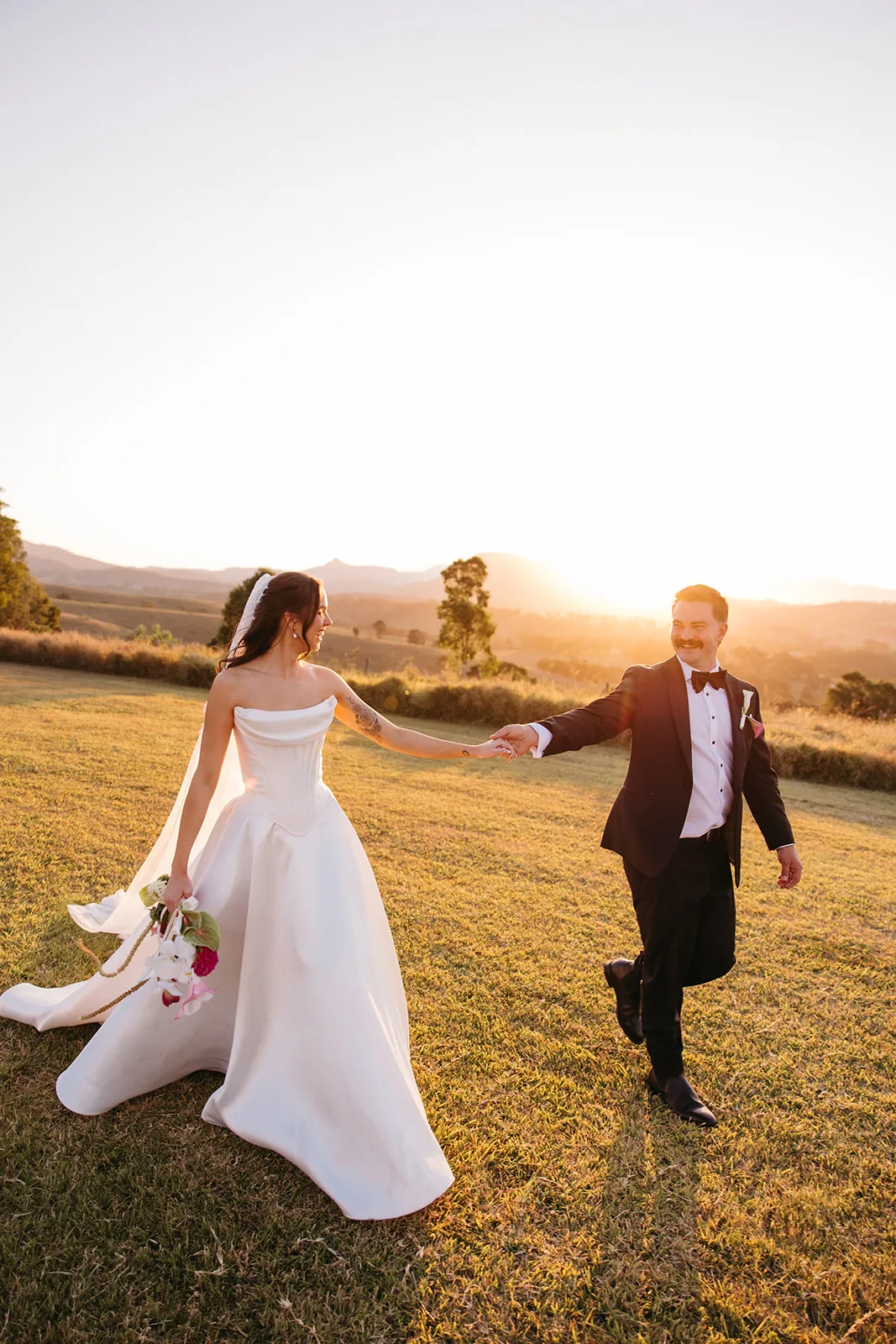 Ally and Braydon holding hands and laughing as they walk across the paddock at sunset