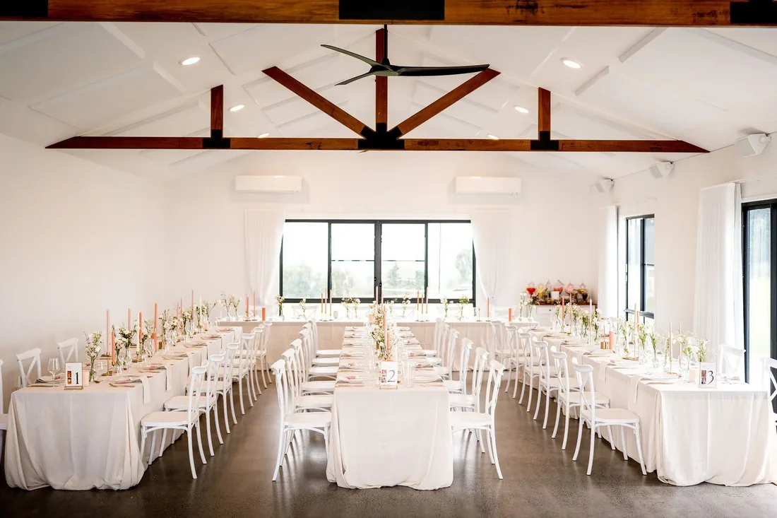 Reception room set with long white-clothed tables and timber beams overhead