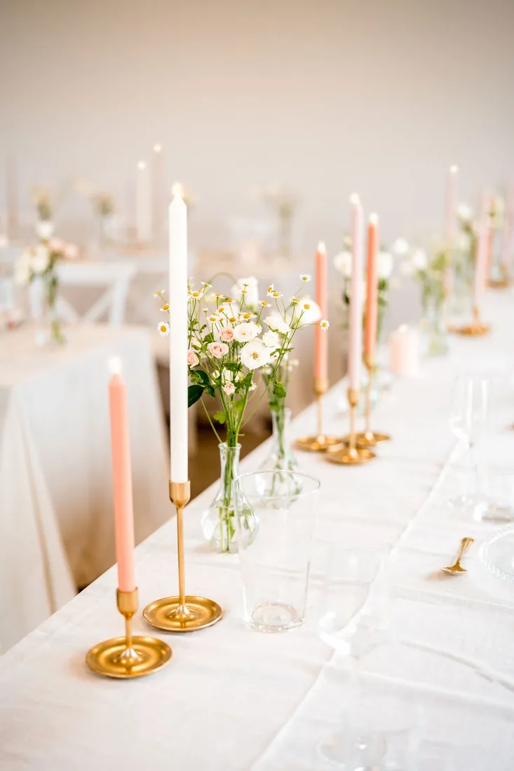 Table setting with brass candlesticks, pink and white taper candles and posies of daisies