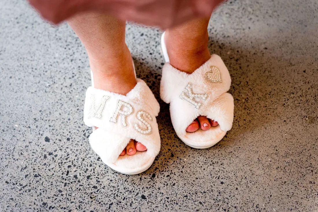 Close-up of white slippers embroidered with Mrs and a heart, worn by the bride