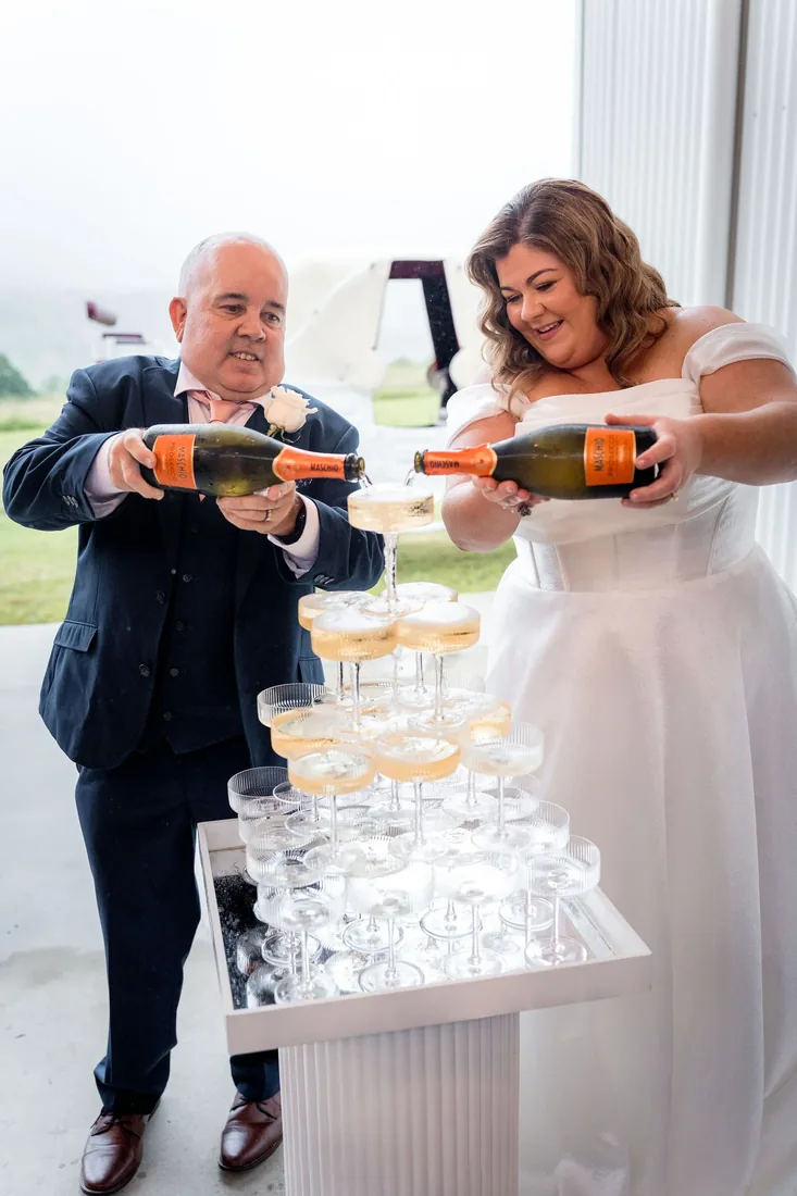 Carrie and Chris pouring champagne into a tower of glasses together