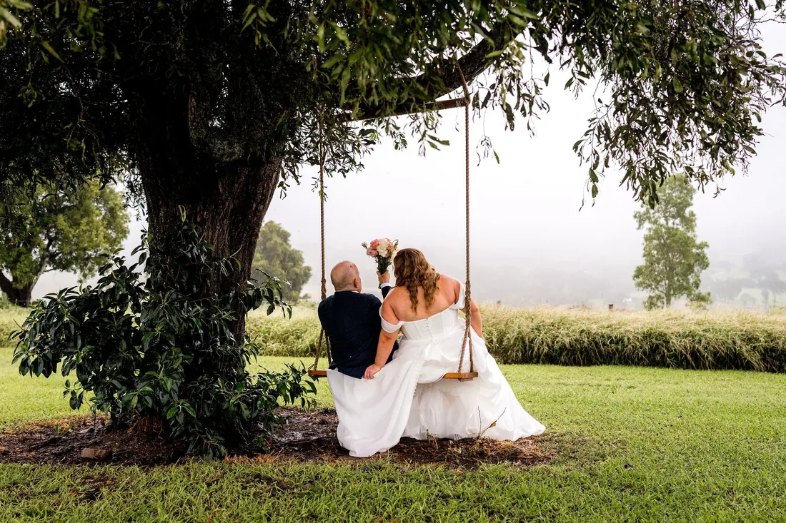 Carrie and Chris sitting together on a tree swing overlooking the misty hills