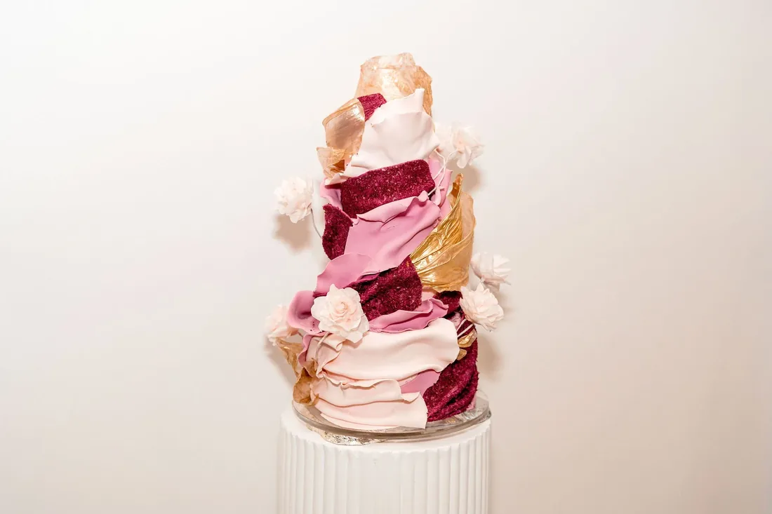 Multi-tiered wedding cake with pink, burgundy and gold sugar drapery and sugar flowers
