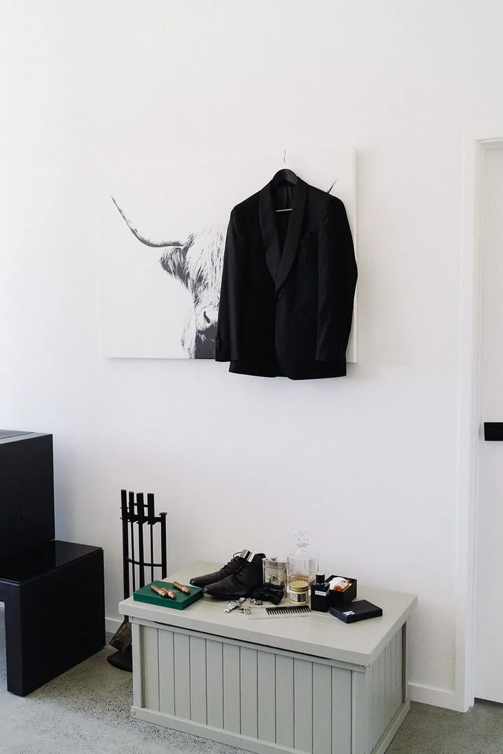 Groom's tuxedo jacket hanging beside a highland cow print, with shoes and grooming accessories styled below