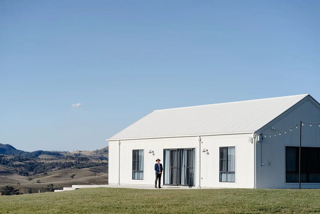 Groom standing outside the white barn-style reception venue with Scenic Rim mountain views