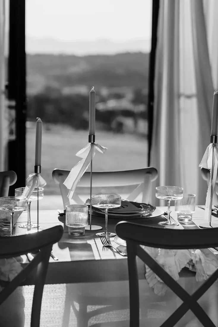 Black and white photo of a reception table set with taper candles and glassware, mountains visible through the doors