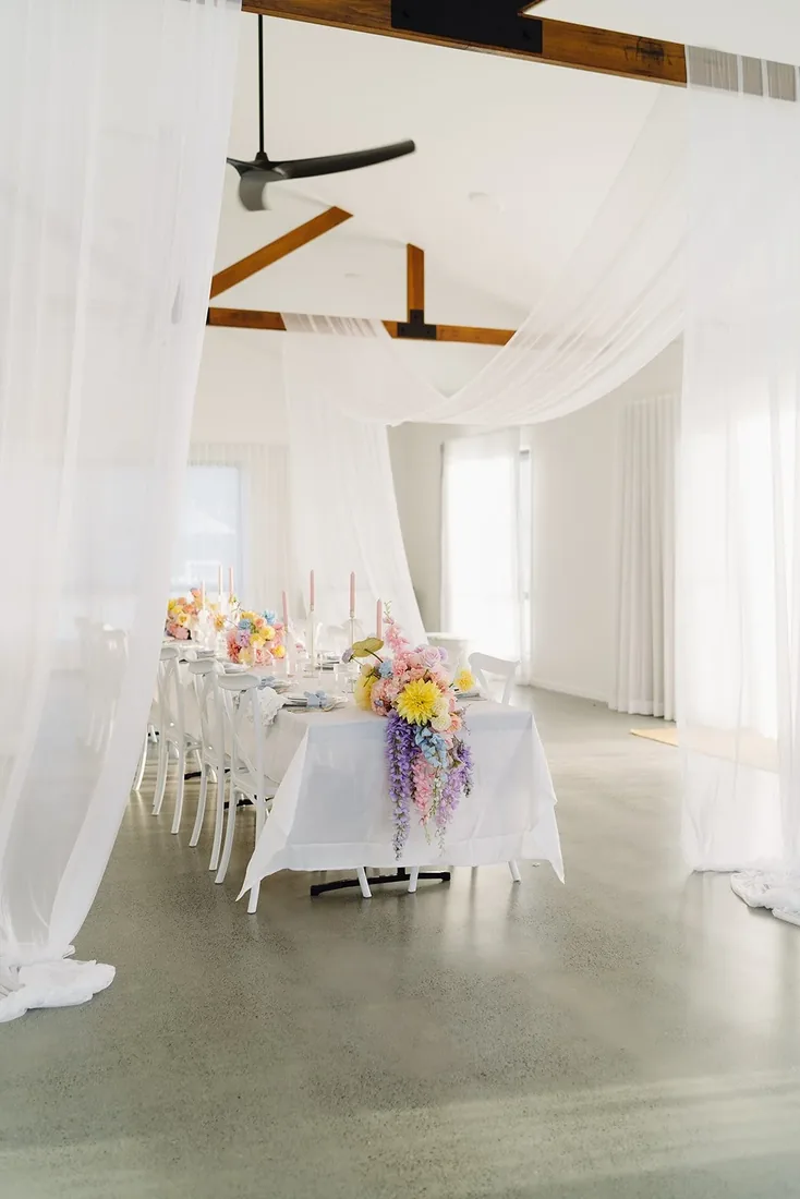 Reception table draped in sheer white fabric with a cascading pastel floral runner