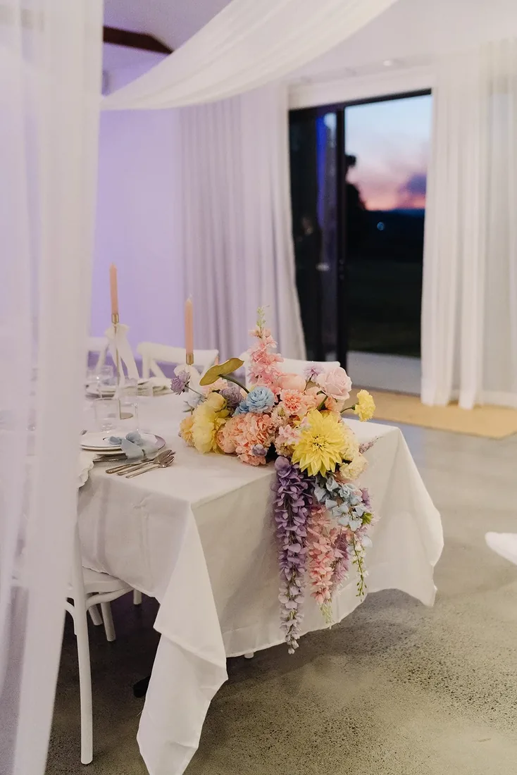 Twilight photo of the reception table with a cascading pastel floral arrangement and sunset through the doors