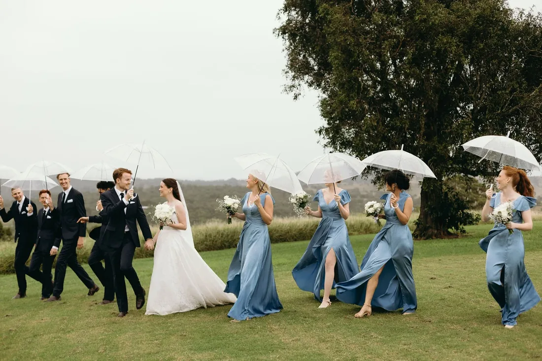 Bridal party walking together with umbrellas raised, Daniel and Emily leading the way