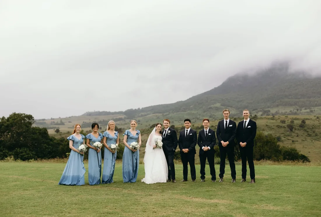 Full bridal party group photo with bridesmaids in dusty blue, misty mountain backdrop