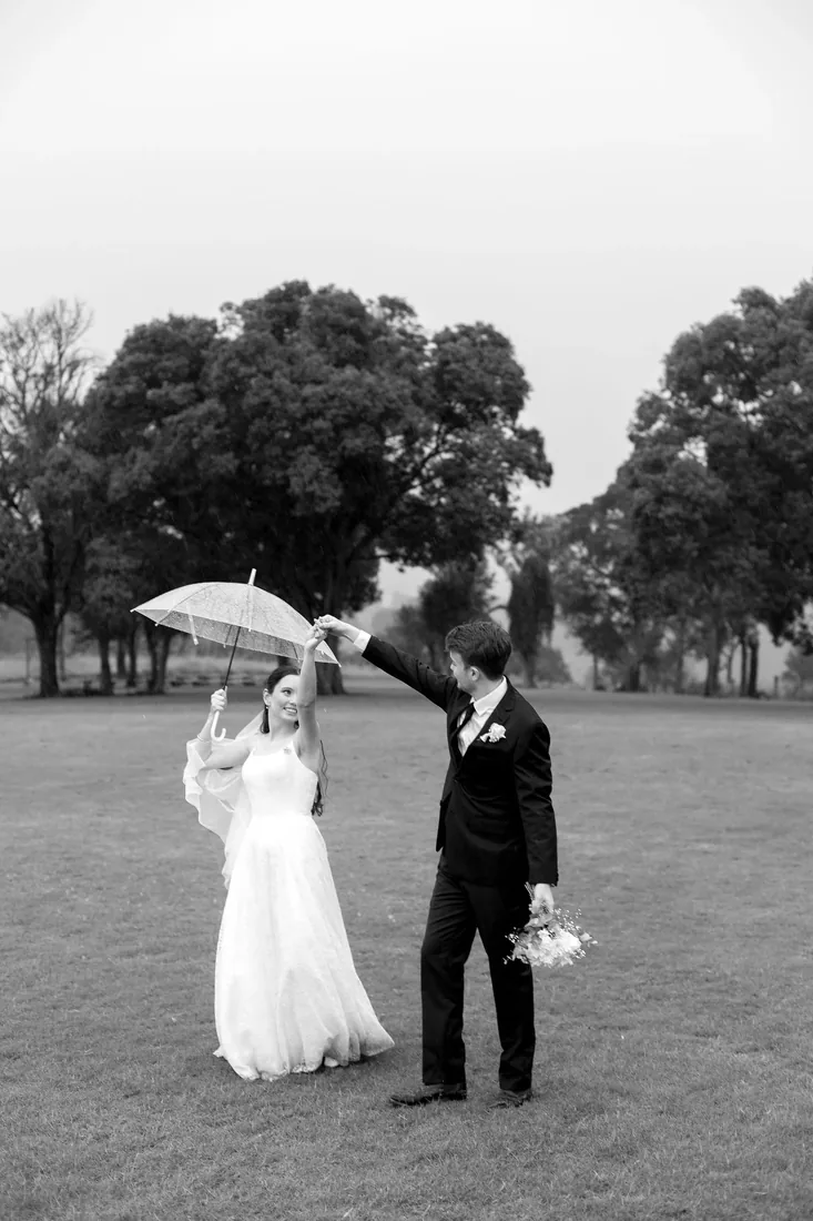 Black and white photo of Daniel holding an umbrella over Emily as they dance in the rain