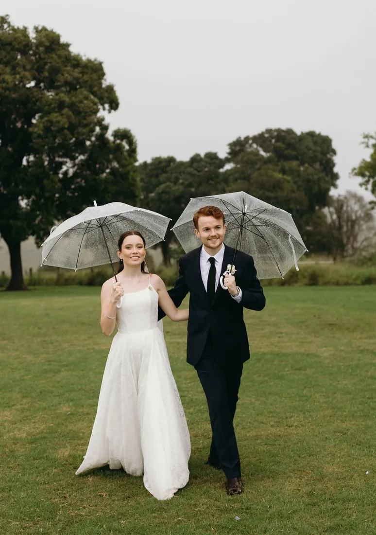 Daniel and Emily walking together, each holding a clear umbrella, mist over the paddocks