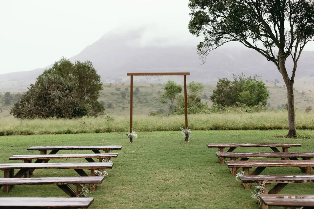 Empty ceremony seating with timber benches and a wooden arch, misty mountain backdrop
