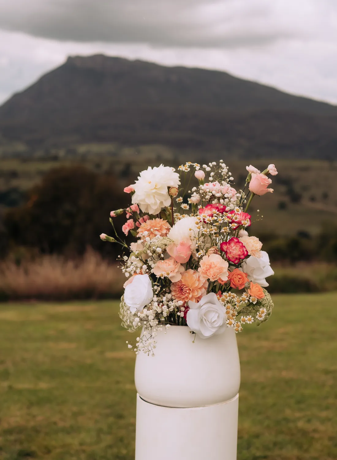 Close-up of a peach, white and pink floral arrangement on a white plinth, mountain behind