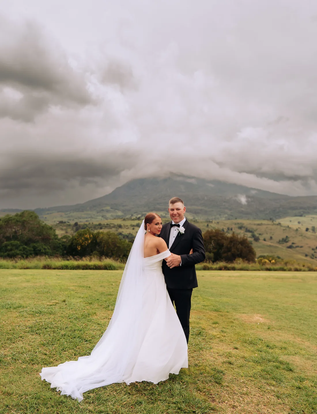 Deanna and Michael embracing on the lawn beneath dramatic storm clouds