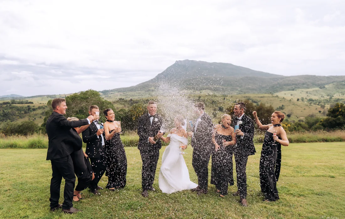 Bridal party spraying champagne and celebrating together, mountain behind