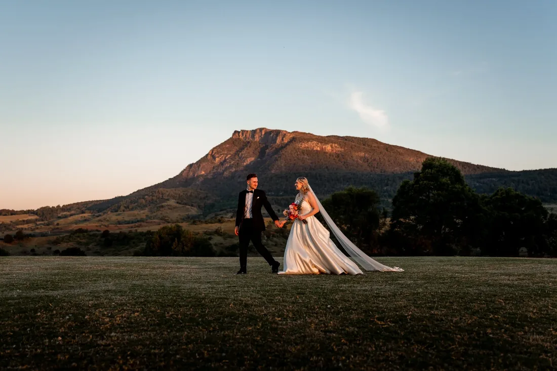 Gabi and Alec walking hand in hand across the lawn at golden hour, mountain backdrop