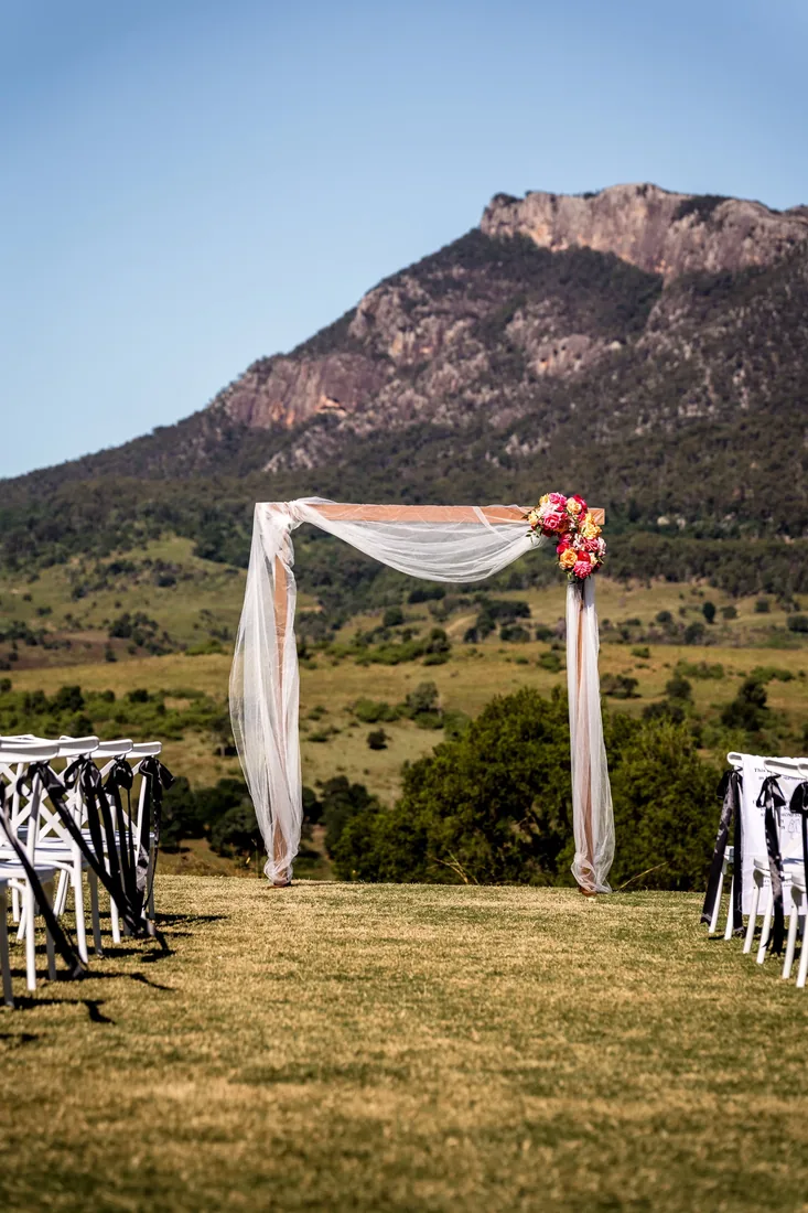 Sheer-draped ceremony arbour with a vibrant floral arrangement, mountain views behind