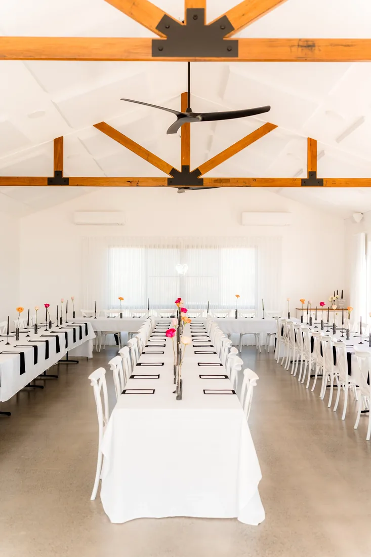 Reception room set with long white tables, black taper candles and bright pink floral accents