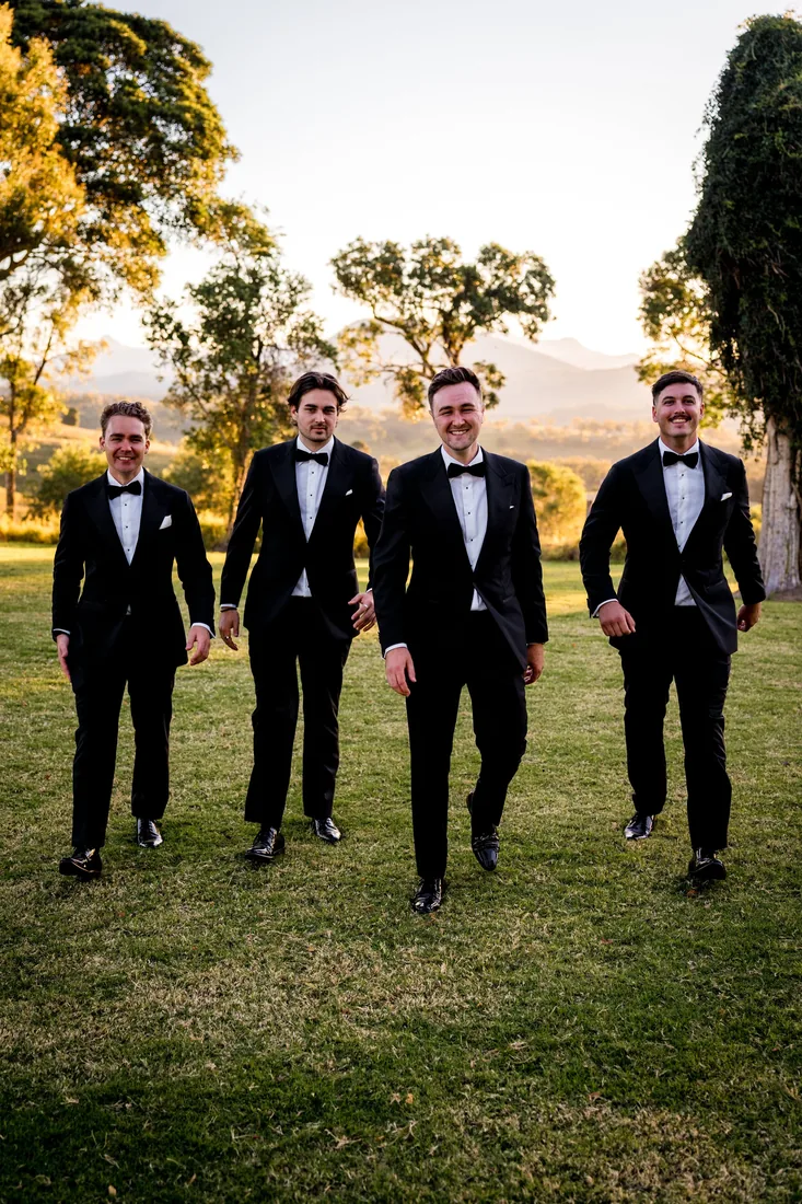 Four groomsmen in black tuxedos walking across the lawn together