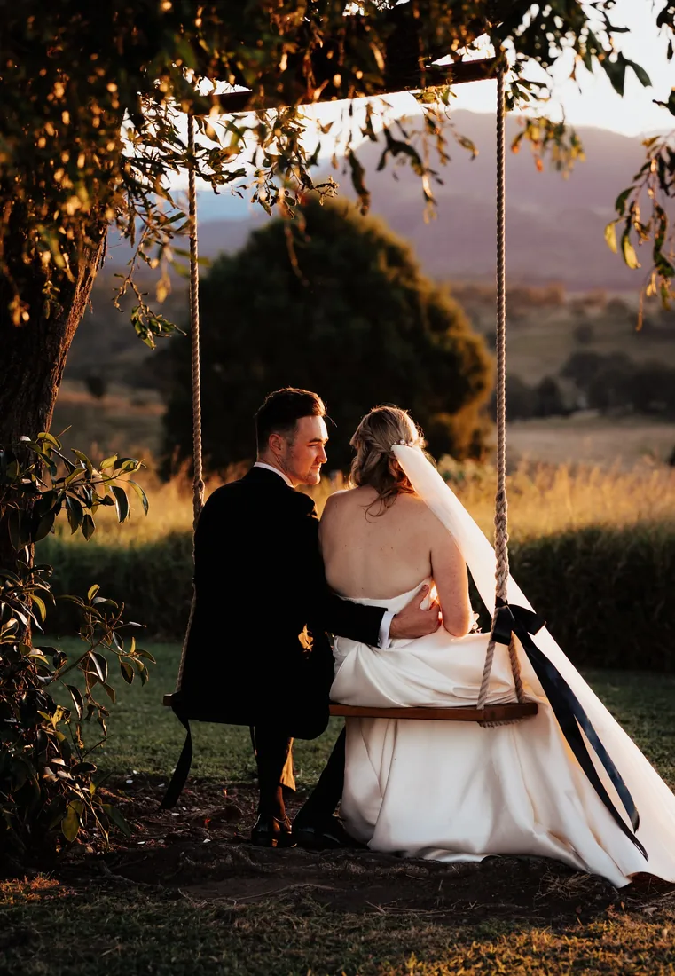 Gabi and Alec sitting together on a tree swing overlooking the hills at dusk