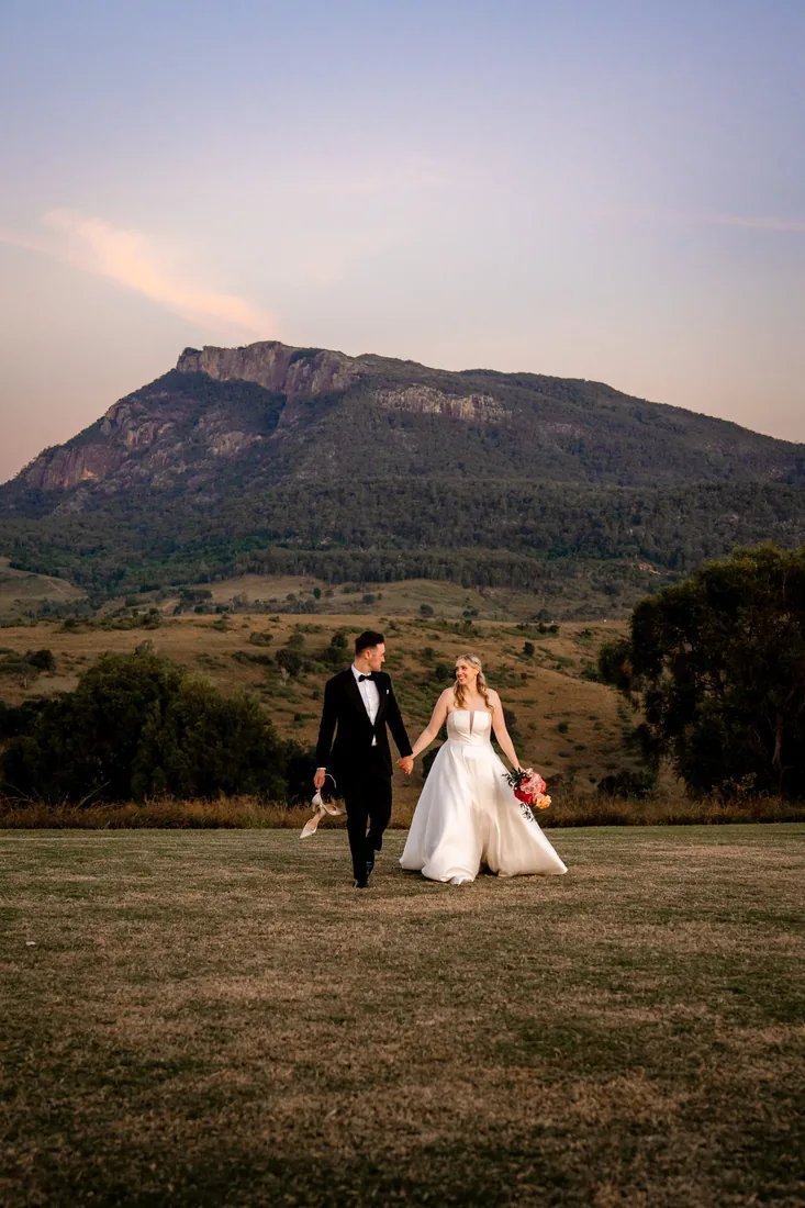 Gabi and Alec walking hand in hand across the lawn with mountain views at dusk
