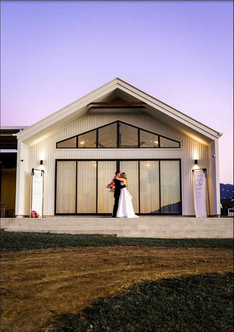 Gabi and Alec kissing at twilight in front of the venue at Maroon Hill Estate