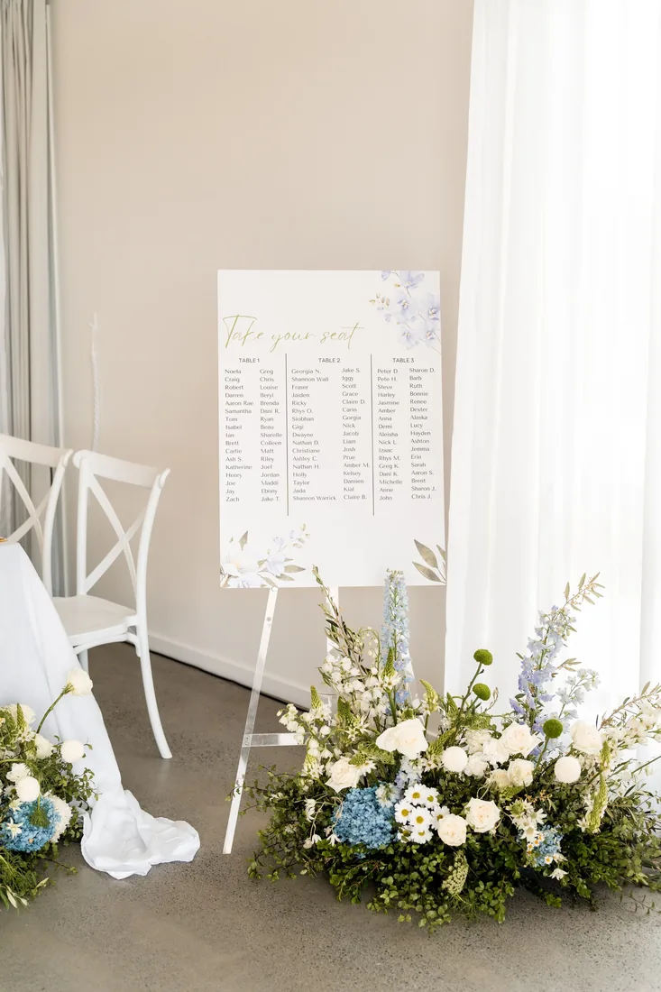 Seating chart sign styled beside blue and white floral arrangements near the ceremony