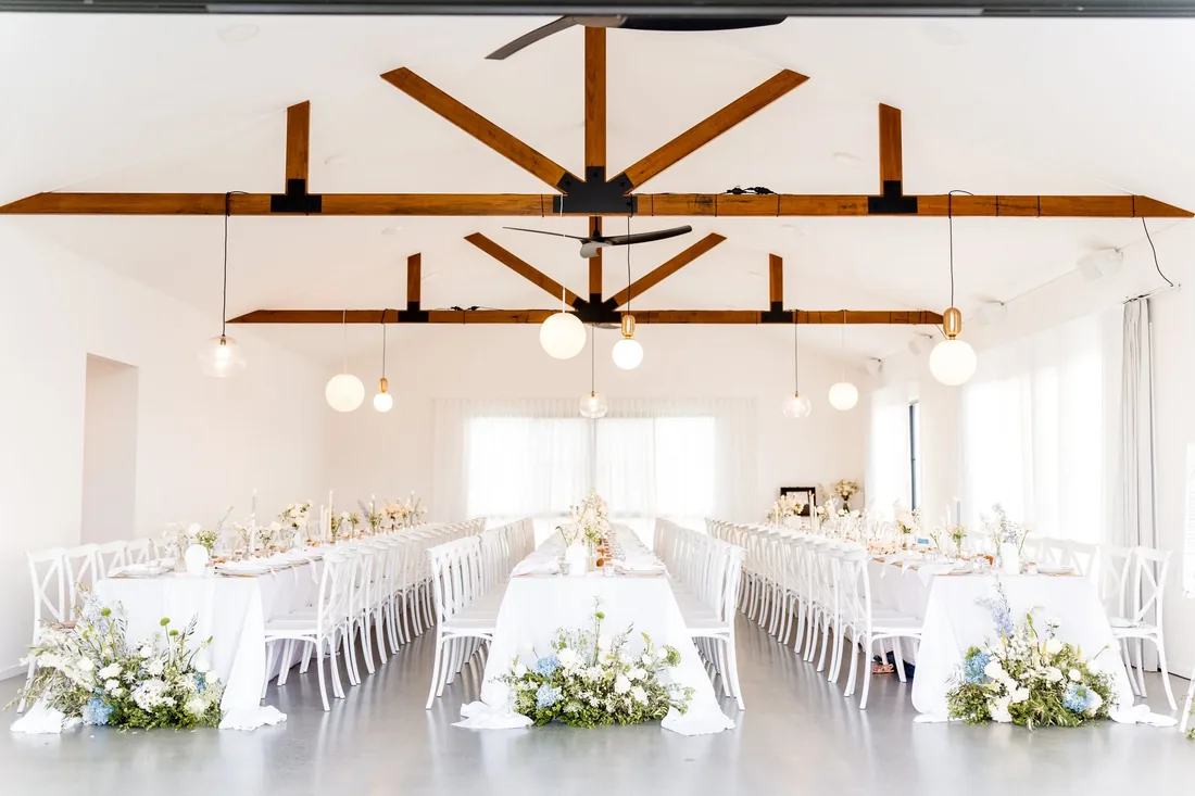 Reception room set with long tables, pendant lighting and exposed timber beams, blue and white floral runners
