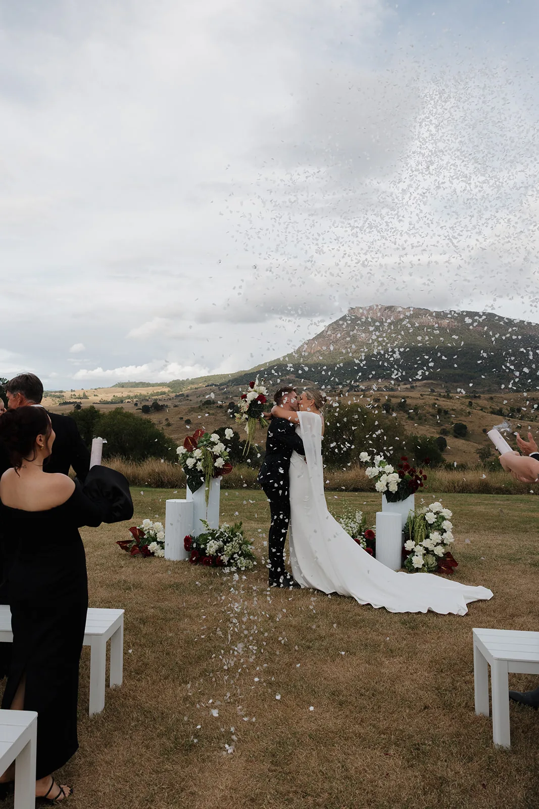Jess and Cory kissing as confetti falls, mountain backdrop
