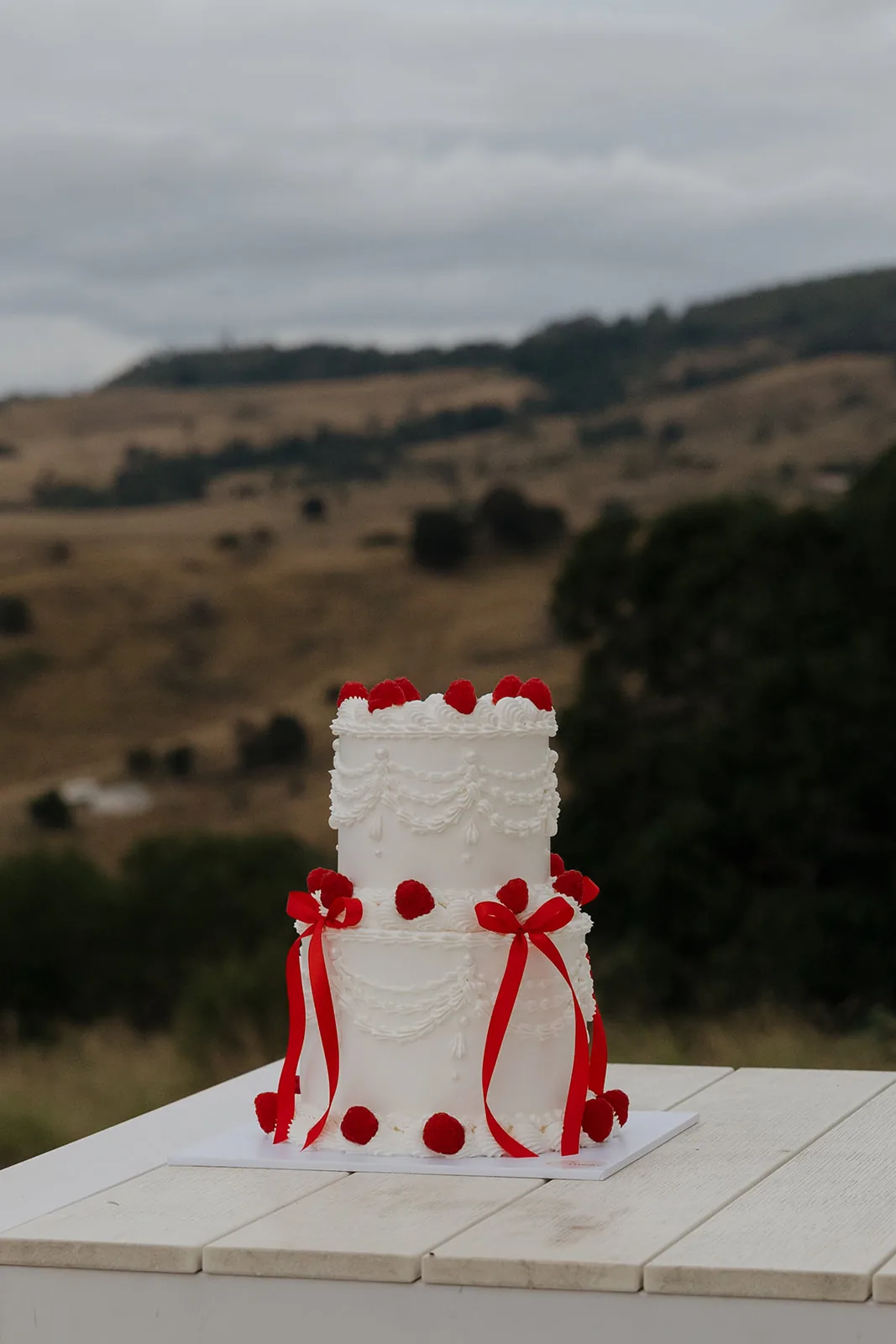 Two-tiered wedding cake with sugar drapery, red ribbons and fresh raspberries
