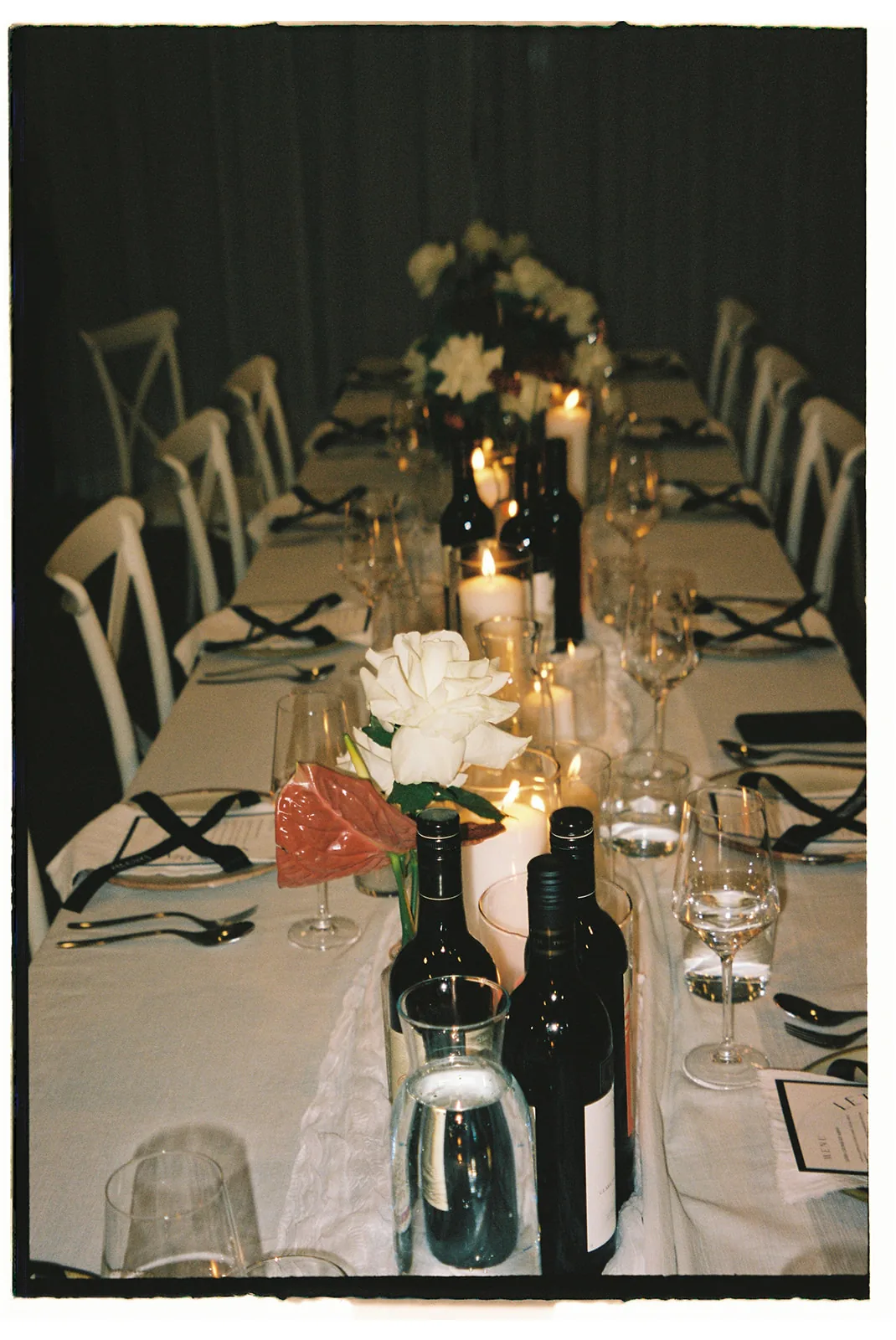 Long reception table set with candles, wine bottles and white roses at night