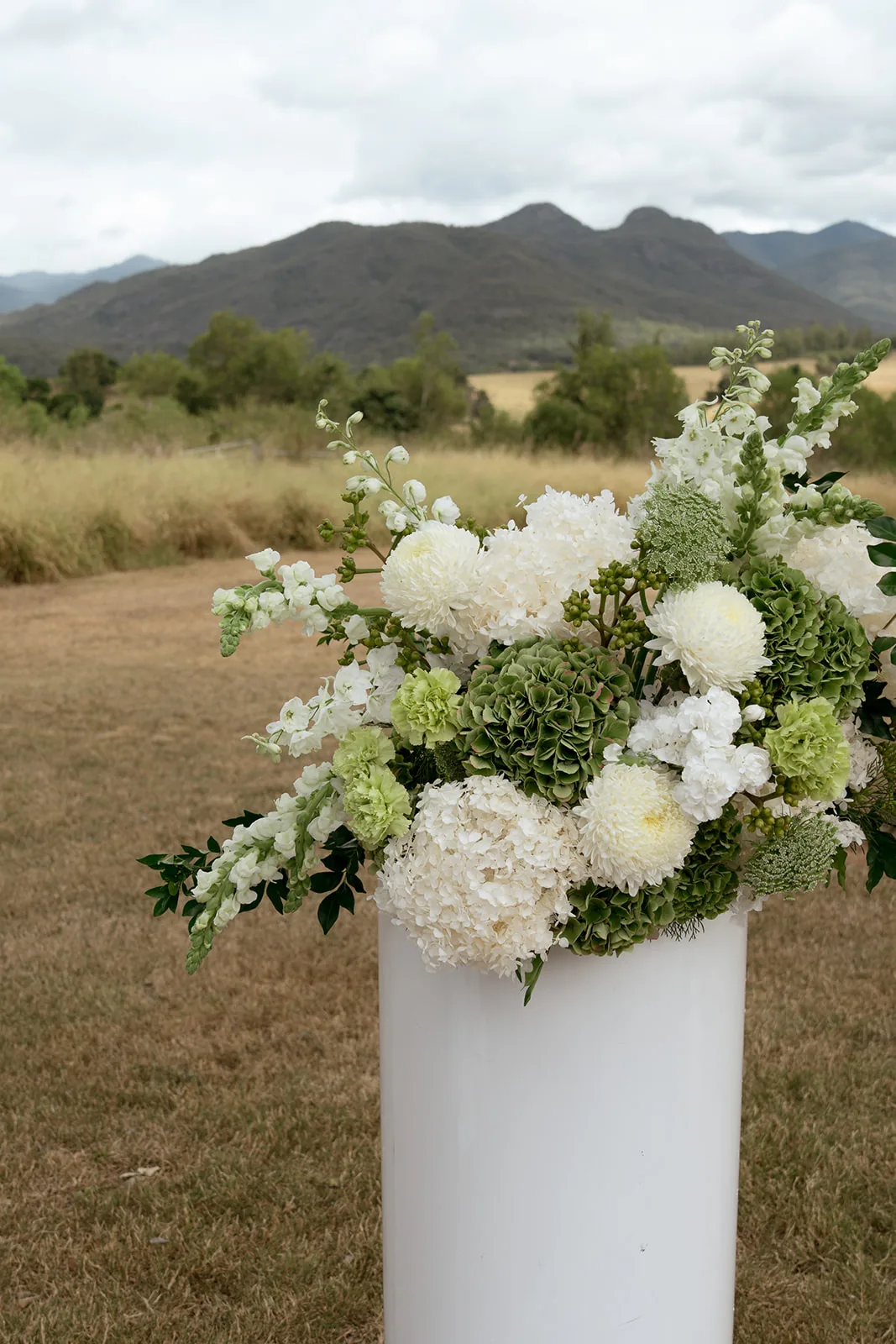White and green floral arrangement in a tall vase, mountain views behind