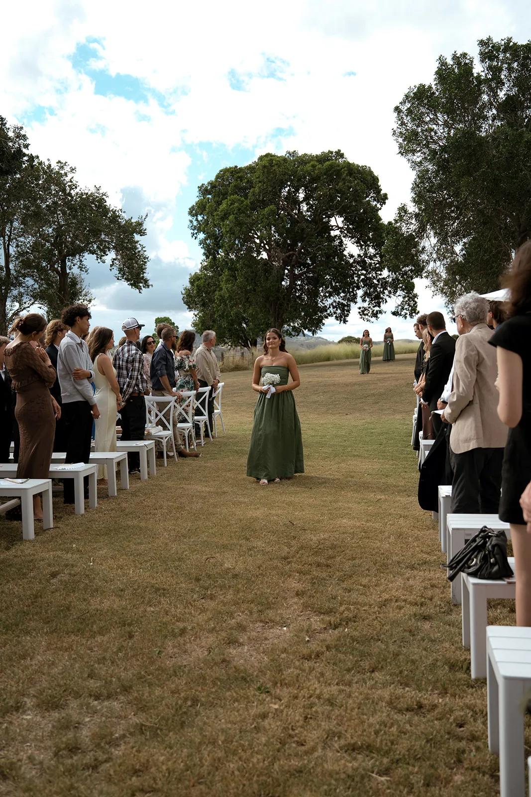 Bridesmaid in a sage green gown walking down the aisle, mountains in the distance