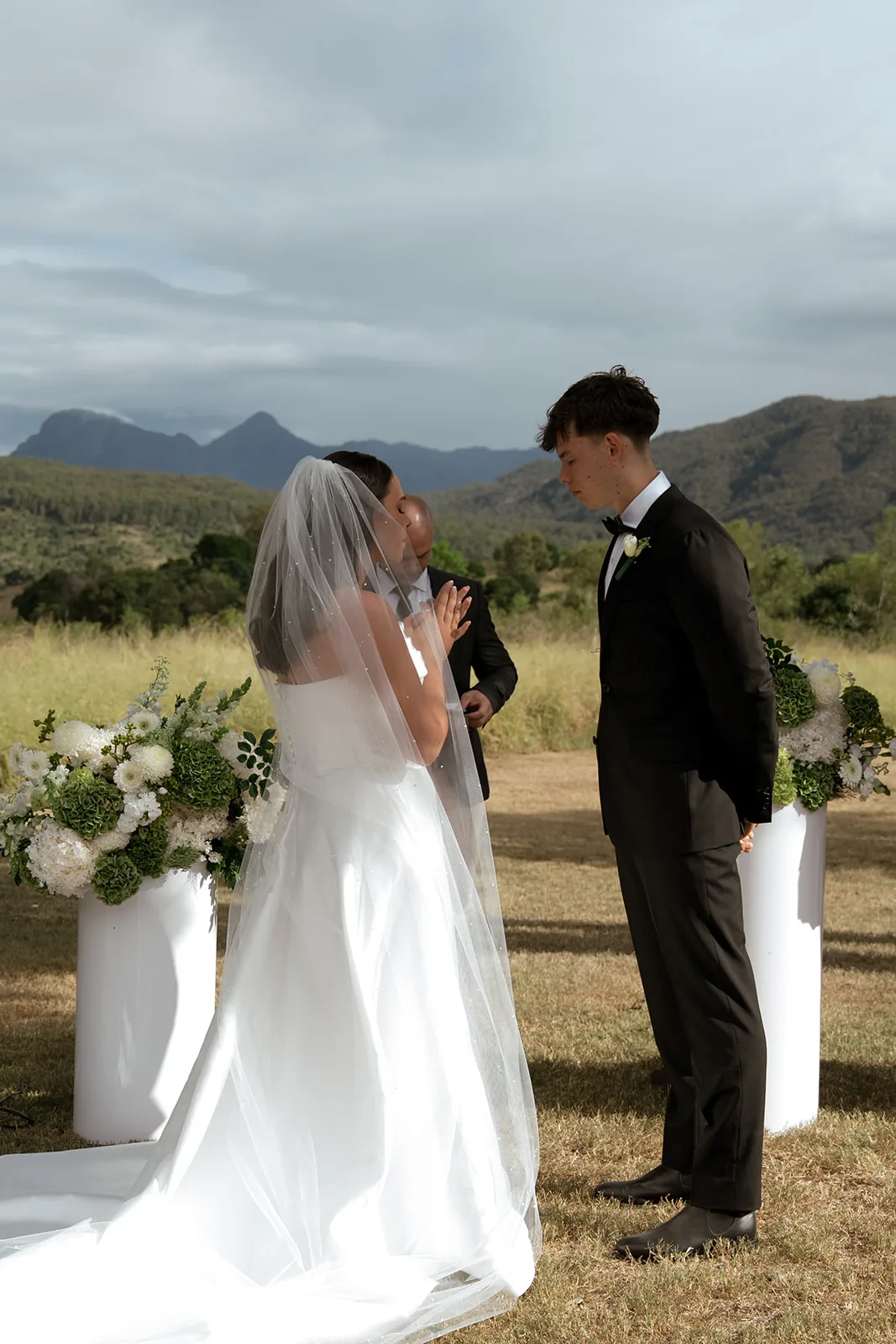 Bride and groom holding hands during their vows, celebrant behind them, mountain views