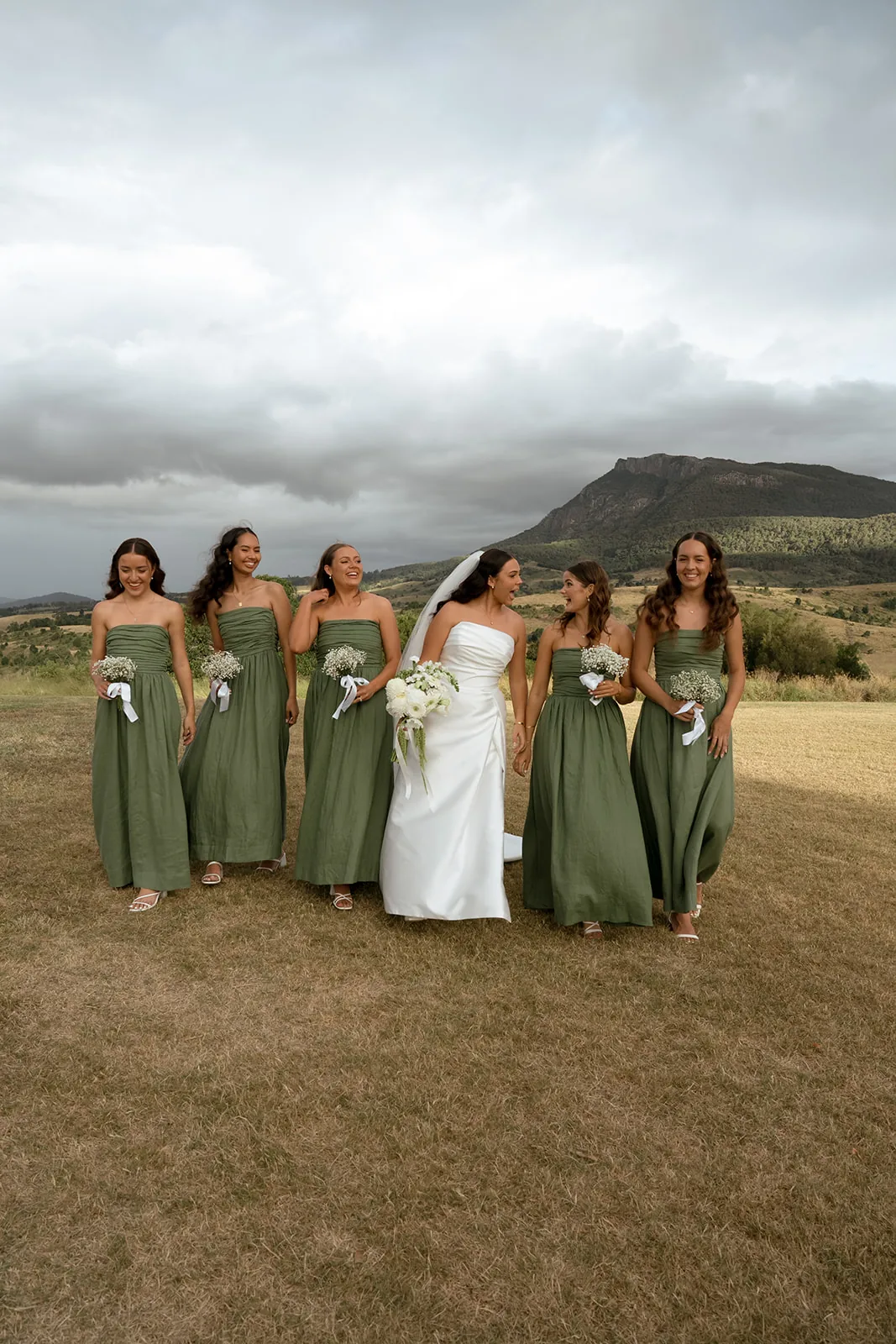 Bride walking with her four bridesmaids in sage green gowns, mountains behind