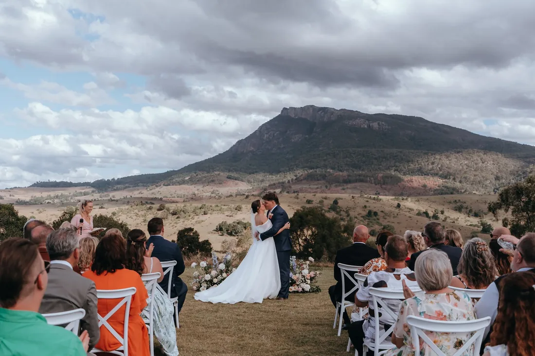 Jorjia and James kissing during their ceremony at Maroon Hill Estate, with Mount Maroon behind them