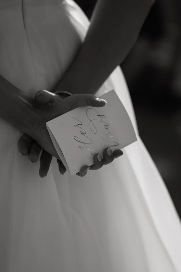 Black and white detail shot of the bride holding her vows behind her back