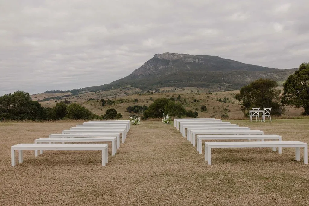 Rows of white benches arranged for the ceremony on the lawn, mountain in the distance