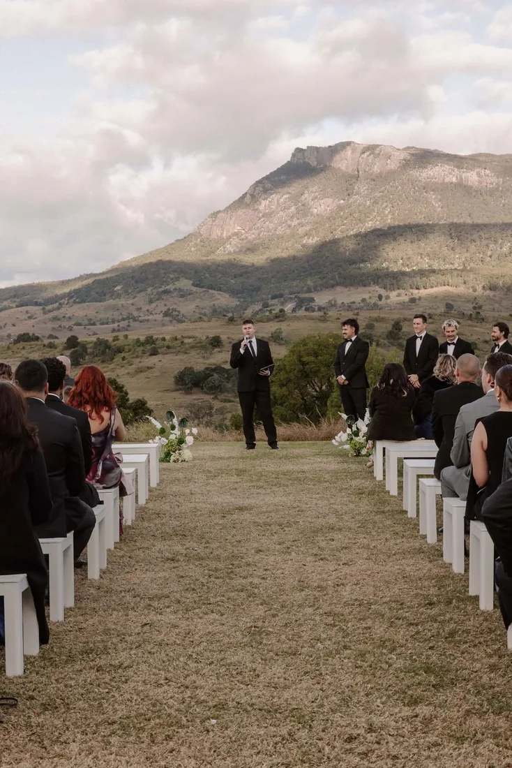 Guest giving a reading during the ceremony, groomsmen standing behind with mountains beyond