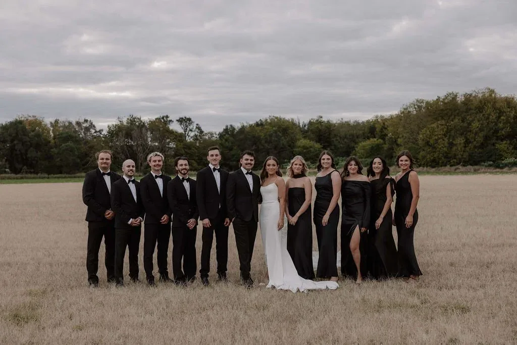 Full bridal party group photo standing in the field under an overcast sky