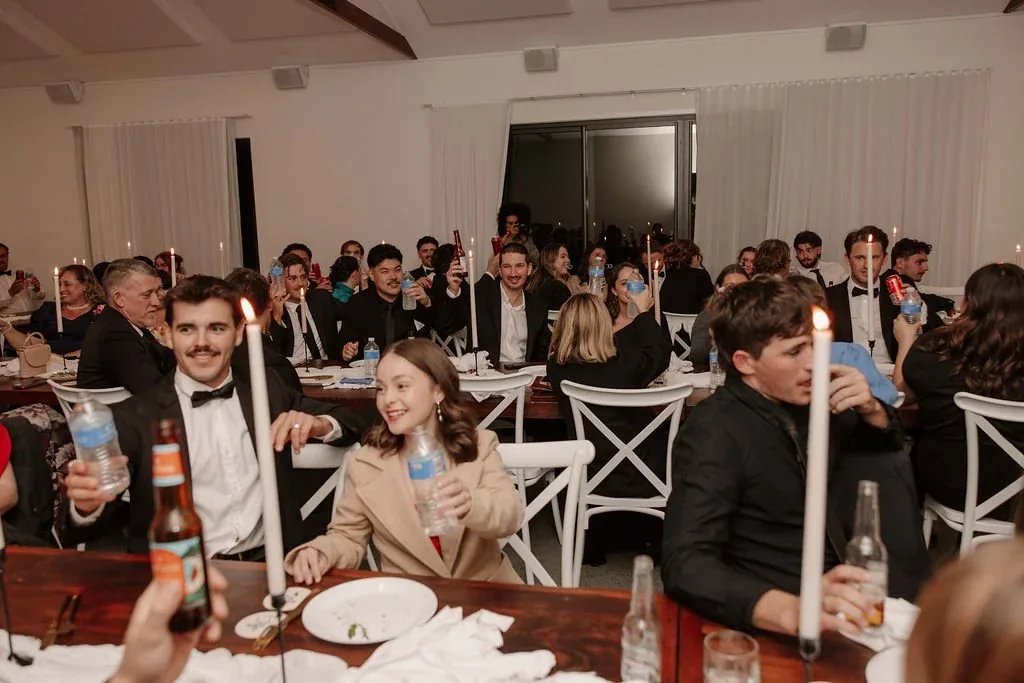 Reception guests raising drinks and toasting around candlelit tables at night